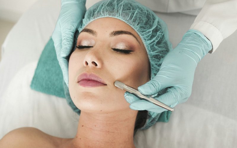 Esteticista con guantes realizando una limpieza facial a una clienta tumbada en la camilla