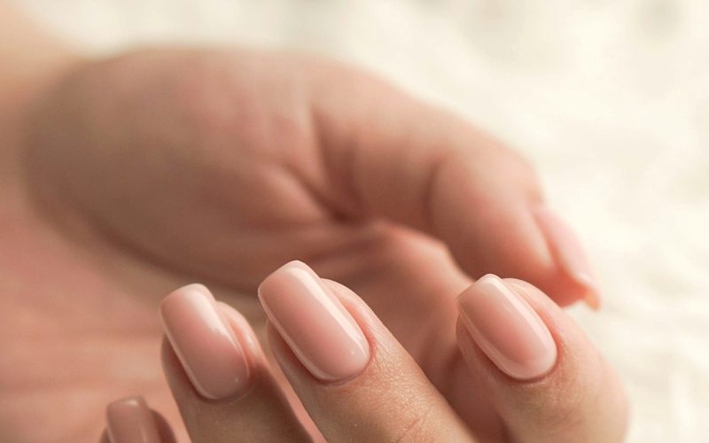 Mano con manicura semipermanente en tono rosa nude sobre una superficie clara