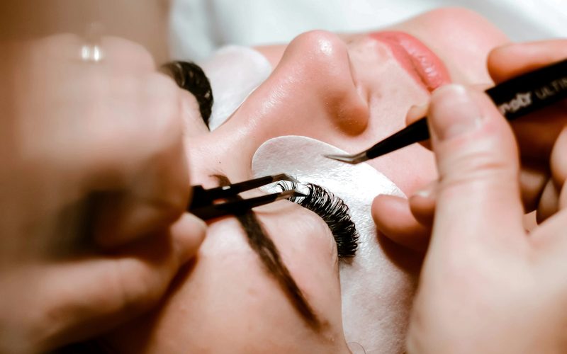 Profesional aplicando extensiones de pestañas pelo a pelo a una clienta con los ojos cerrados