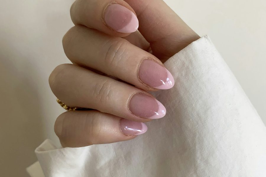 Mano con las uñas pintadas en rosa nude sujetando una tela blanca