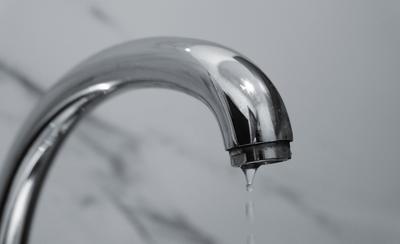 Caño cromado de un grifo con una gota de agua a punto de caer