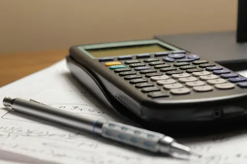 Calculadora y portaminas sobre hojas con cifras encima de una mesa