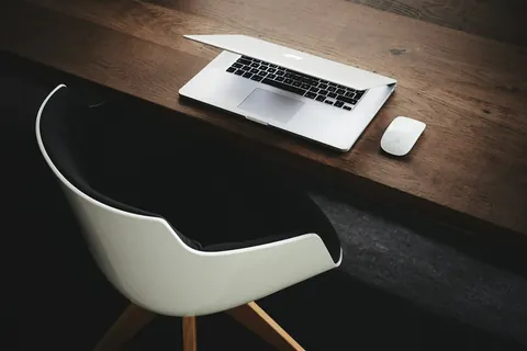 Portátil y ratón sobre un escritorio de madera oscura junto a una silla de oficina
