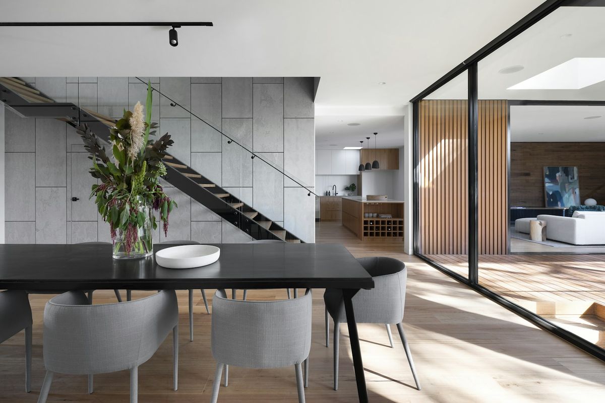 Salón comedor de diseño con mesa larga, cocina abierta y paneles de madera