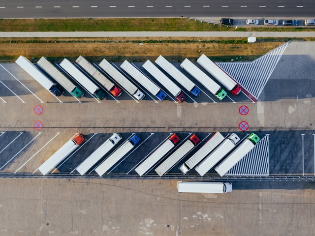 Vista aérea de una fila de semirremolques blancos estacionados en los muelles de carga de una nave logística.