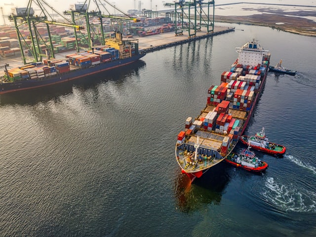 Buque portacontenedores cargado maniobrando en la bocana de un puerto asistido por remolcadores.