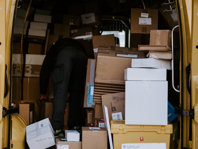 Persona cargando cajas de cartón y bultos en el interior de una furgoneta de reparto amarilla.