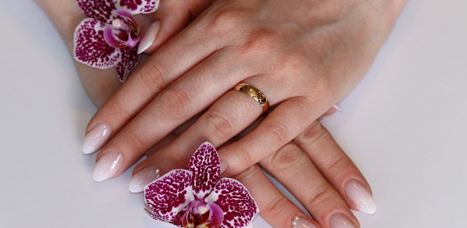 Manos con manicura nude en degradado junto a dos orquídeas