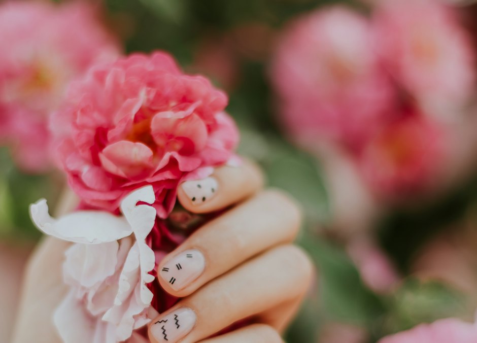 Mano con uñas decoradas con pequeñas flores, sujetando una flor rosa