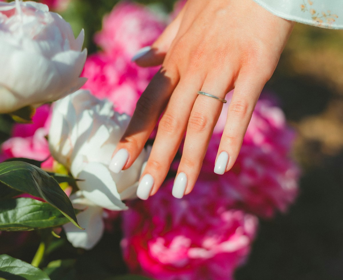 Mano con manicura clara apoyada entre peonías rosas y blancas