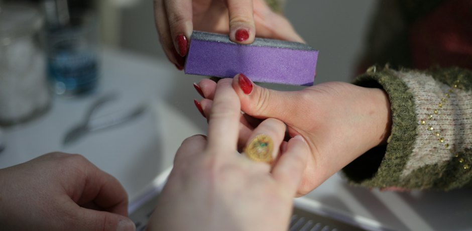 Antes: uña con restos de esmalte rojo mientras se pule con un taco