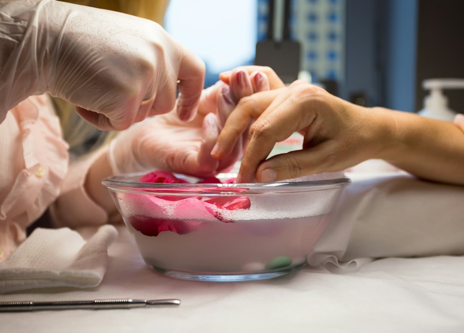 Cuidado: manos en remojo en un bol mientras una manicurista con guantes trabaja las uñas