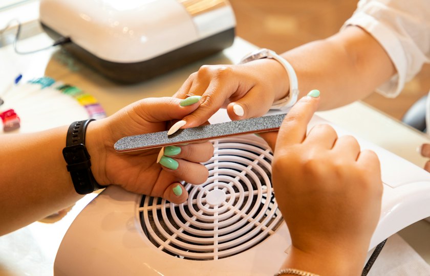 Manicurista limando las uñas de una clienta sobre un aspirador de mesa