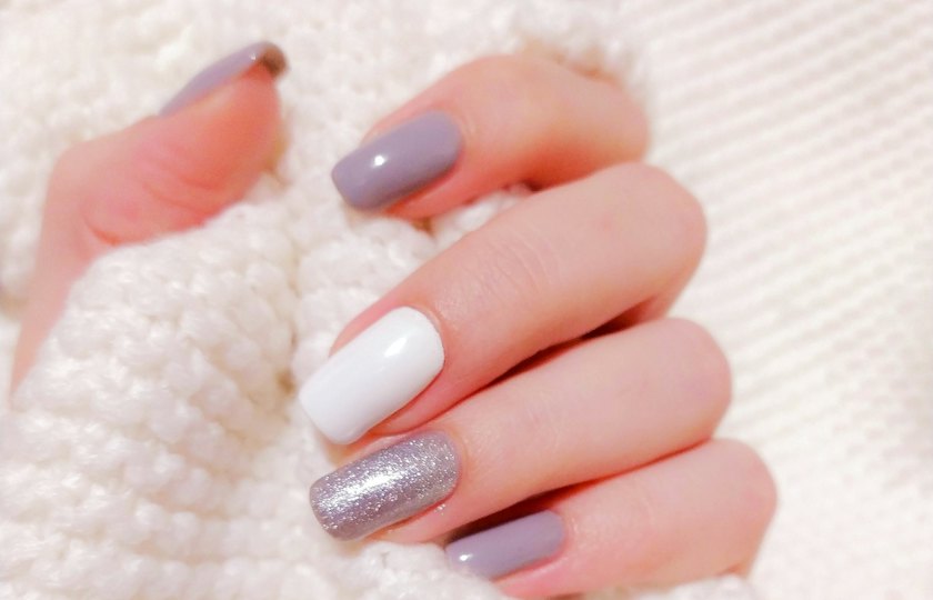 Mano sobre punto blanco con uñas en lila, blanco y purpurina plateada
