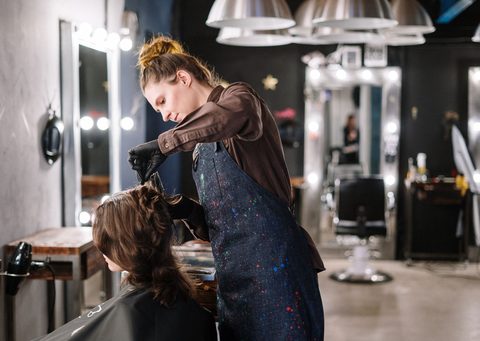 Peluquera secando el pelo de una clienta frente al espejo iluminado de un salón