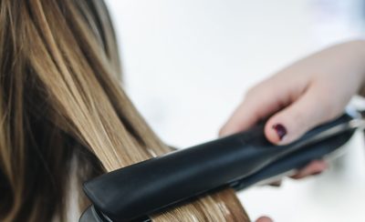 Plancha alisando un mechón de pelo largo y liso sobre fondo claro