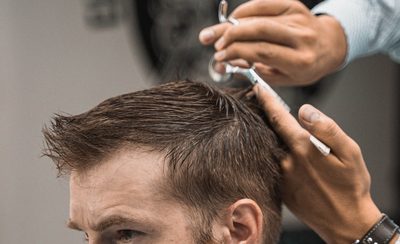 Barbero cortando con tijeras el pelo de un cliente en la zona de barbería