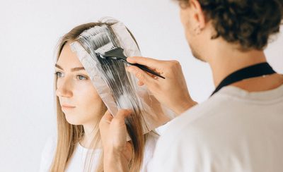 Peluquero aplicando tinte con brocha sobre el pelo largo de una clienta