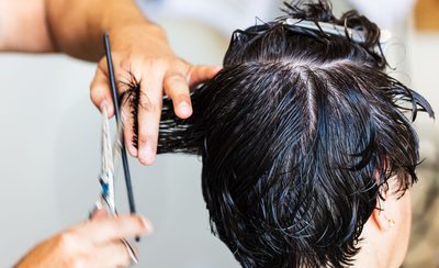 Manos cortando con tijeras y peine el pelo mojado de una persona en el salón