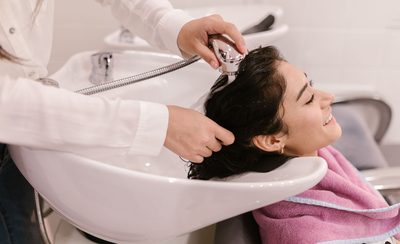 Clienta tumbada en el lavacabezas mientras le aclaran el pelo con la ducha