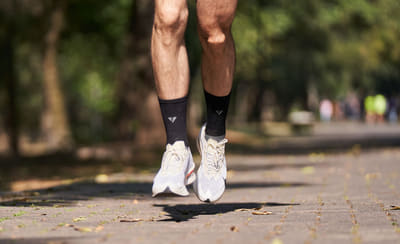 Corredor de espaldas con zapatillas blancas en el aire, corriendo por un camino de parque