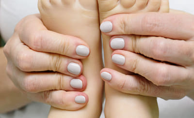 Manos de un adulto sujetando los pies descalzos de un niño sobre fondo claro