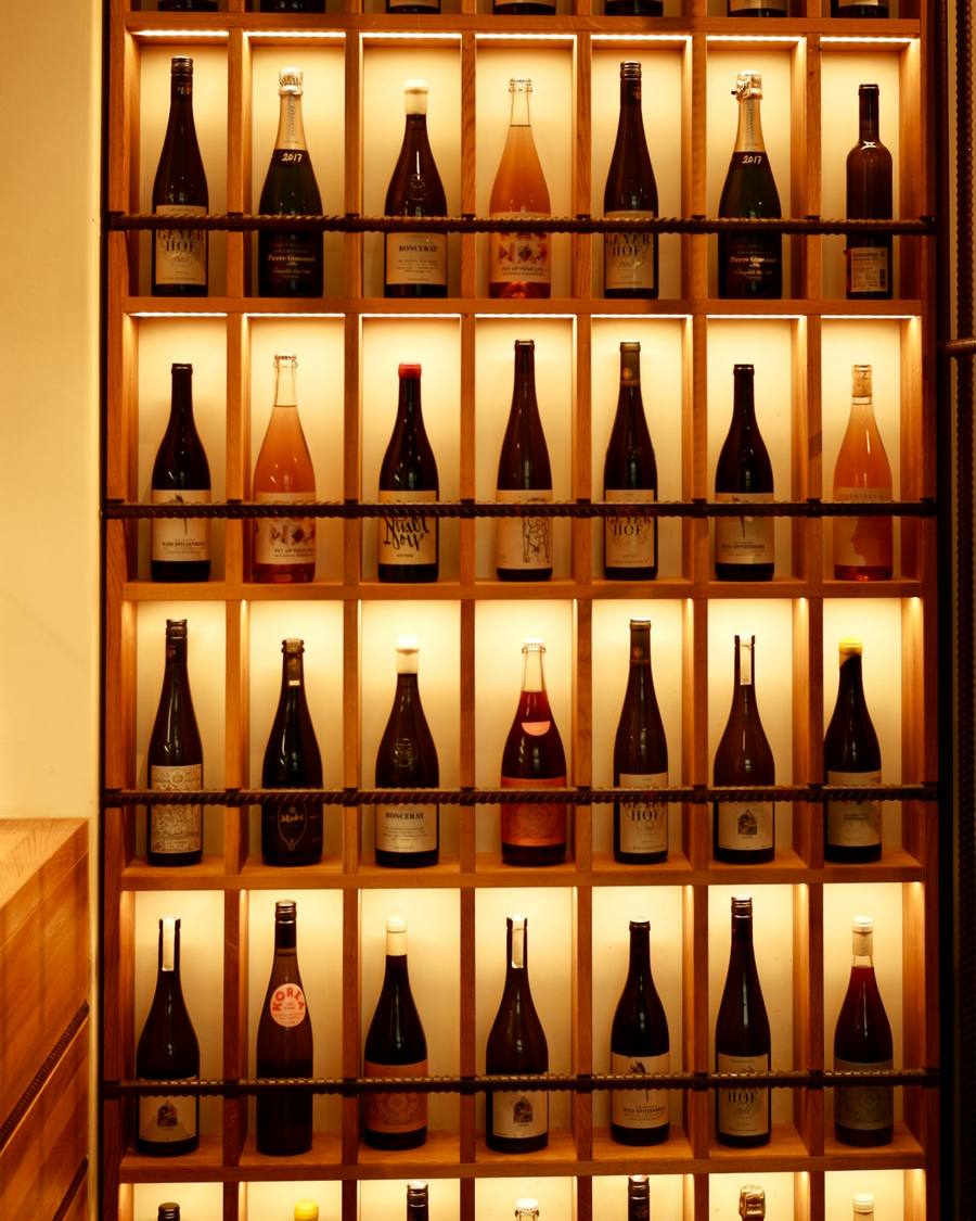 Botellero de madera iluminado desde detrás, lleno de botellas de vino.