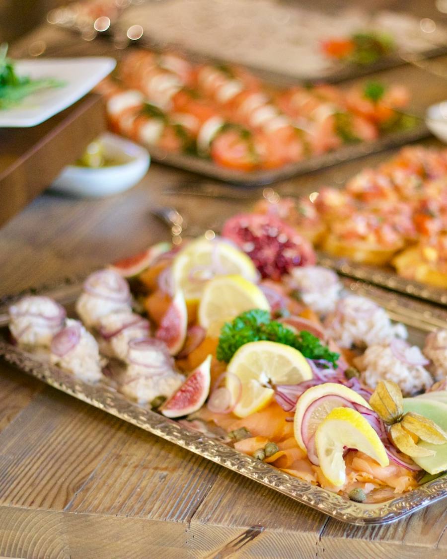 Bandejas con pescado curado, fruta y tostas sobre una mesa de madera.