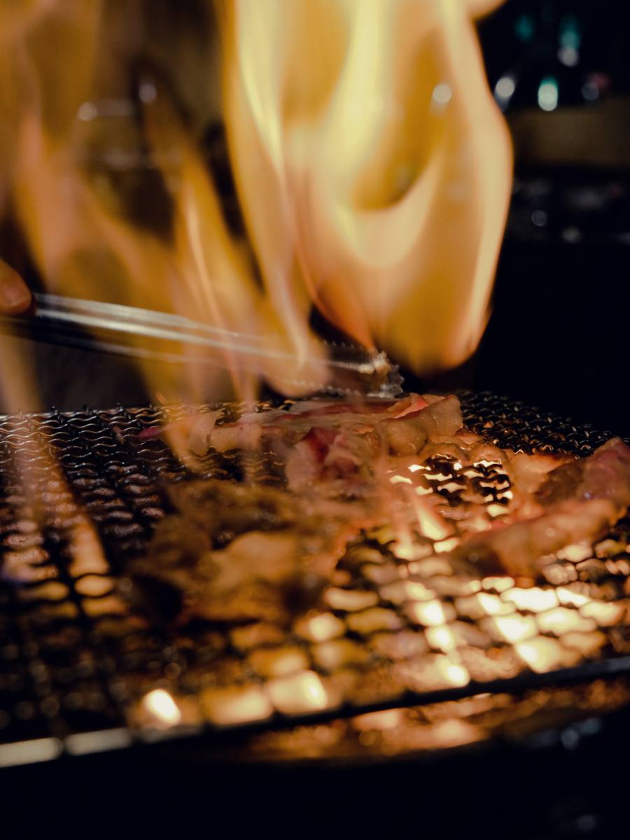 Llamarada sobre una rejilla con carne, envuelta en humo.