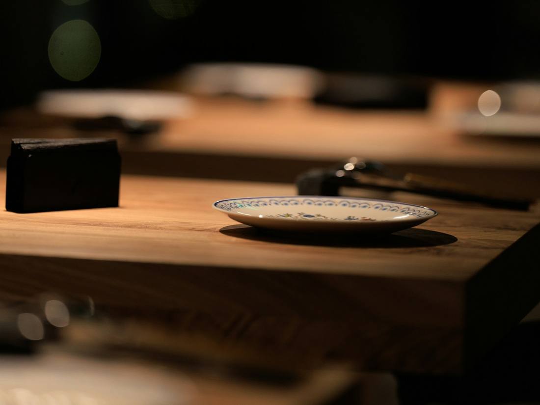 Mesa de madera puesta en una sala oscura, con luces desenfocadas al fondo.