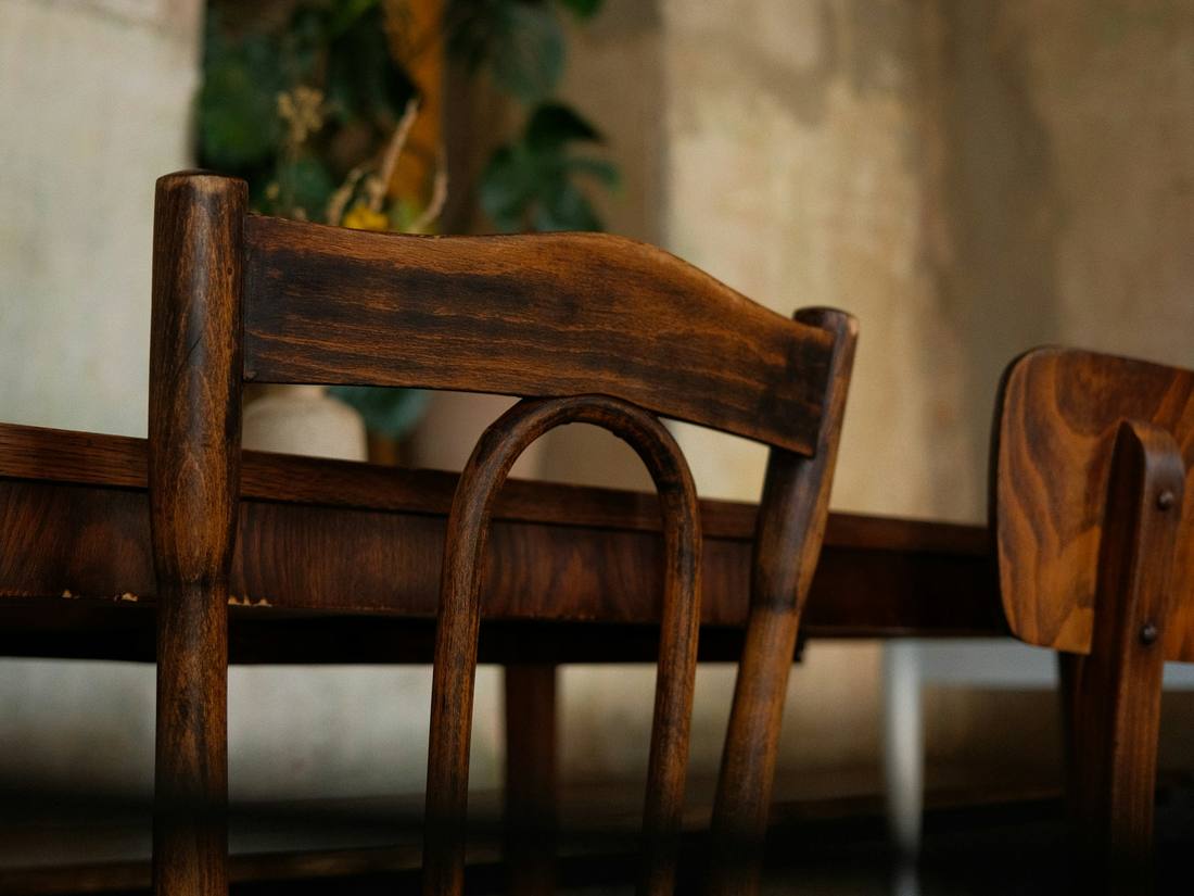 Sillas de madera oscura junto a una mesa, en una sala de paredes de piedra.
