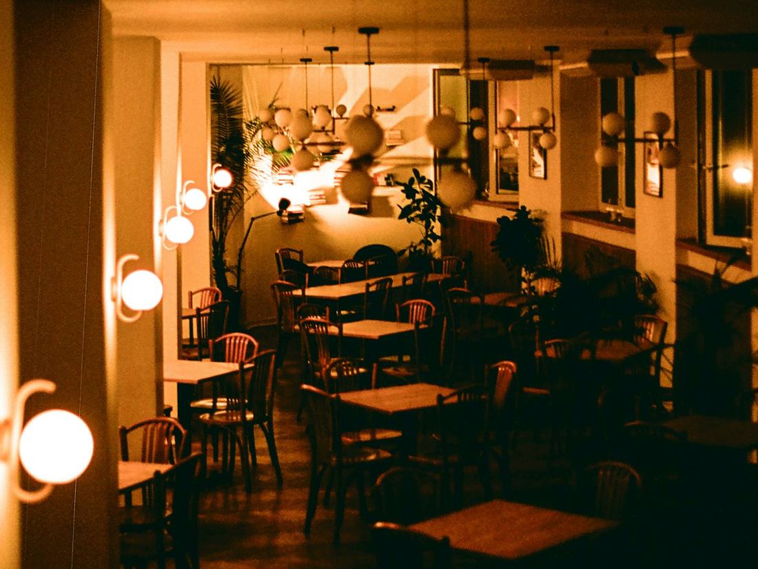 Sala del restaurante en penumbra, con apliques encendidos y mesas vacías.