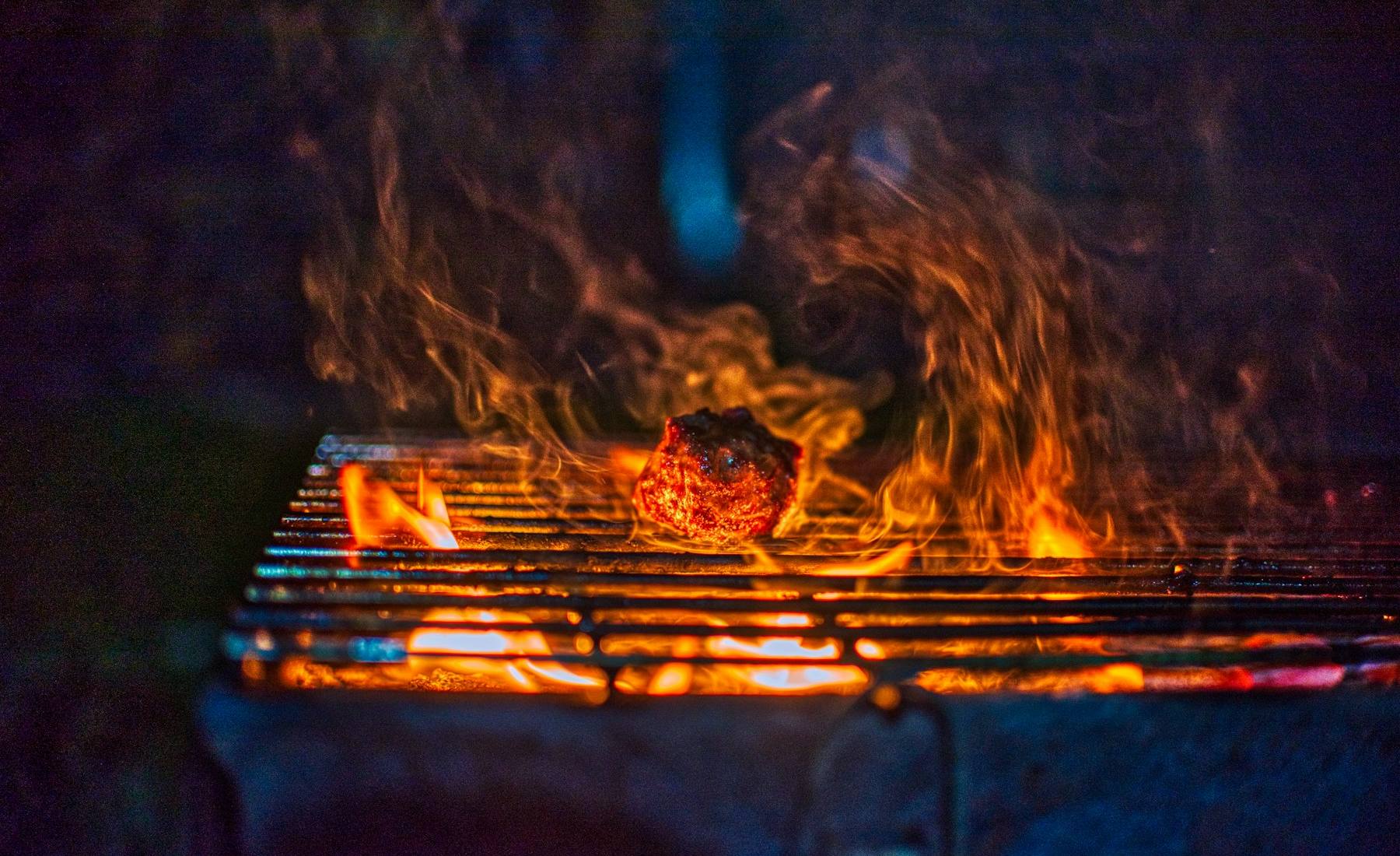 Parrilla de hierro con llamas altas y un corte de carne dorándose sobre las brasas.