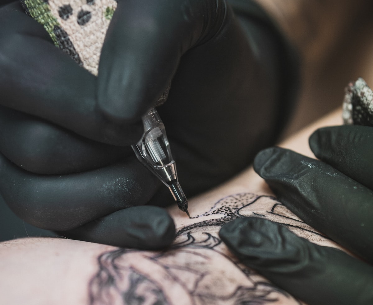 Manos con guantes negros tatuando un brazo con la máquina