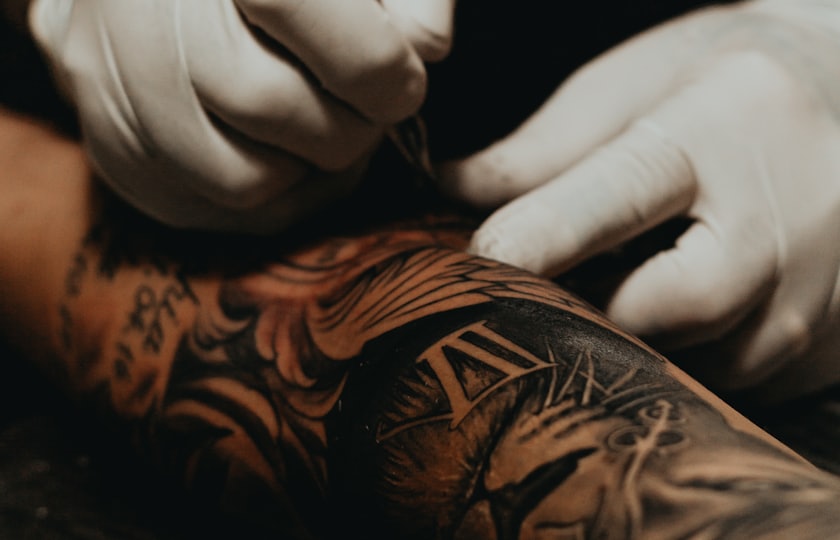 Manos con guantes tatuando el brazo de un cliente