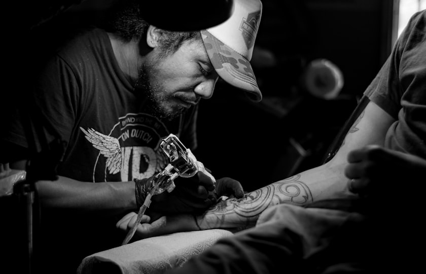 Tatuador trabajando sobre el brazo de un cliente, en blanco y negro