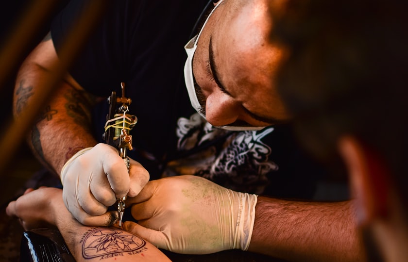 Tatuador con mascarilla tatuando de cerca en el estudio