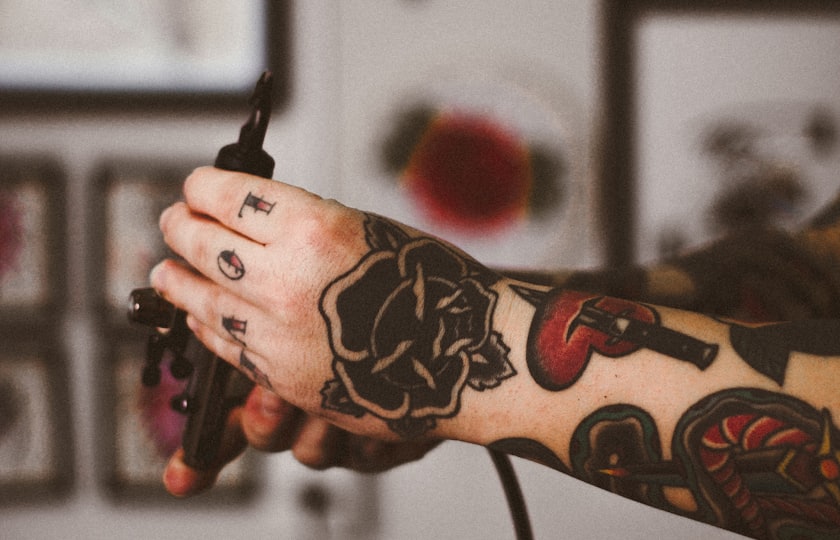 Mano tatuada sujetando una máquina de tatuar en el estudio