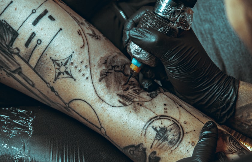 Guante negro tatuando un antebrazo con un diseño de línea