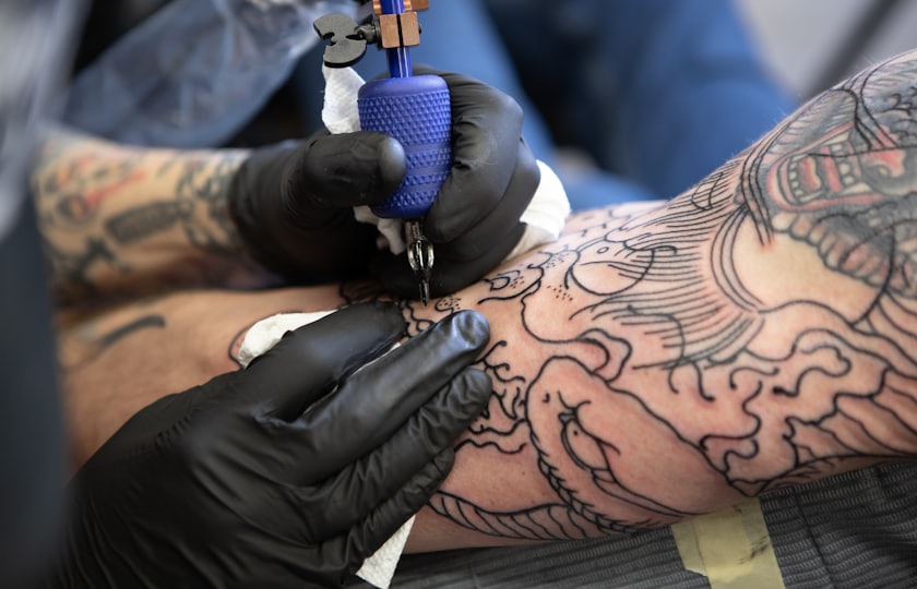 Manos con guantes negros tatuando un brazo con un diseño japonés